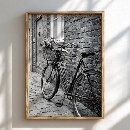 Black and white poster of vintage bicycle leaning against textured brick wall on cobblestone street