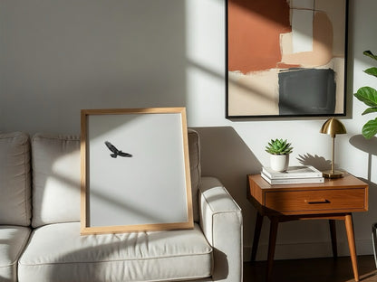 Framed wall decor featuring a black bird in flight against a pale sky with natural wood frame