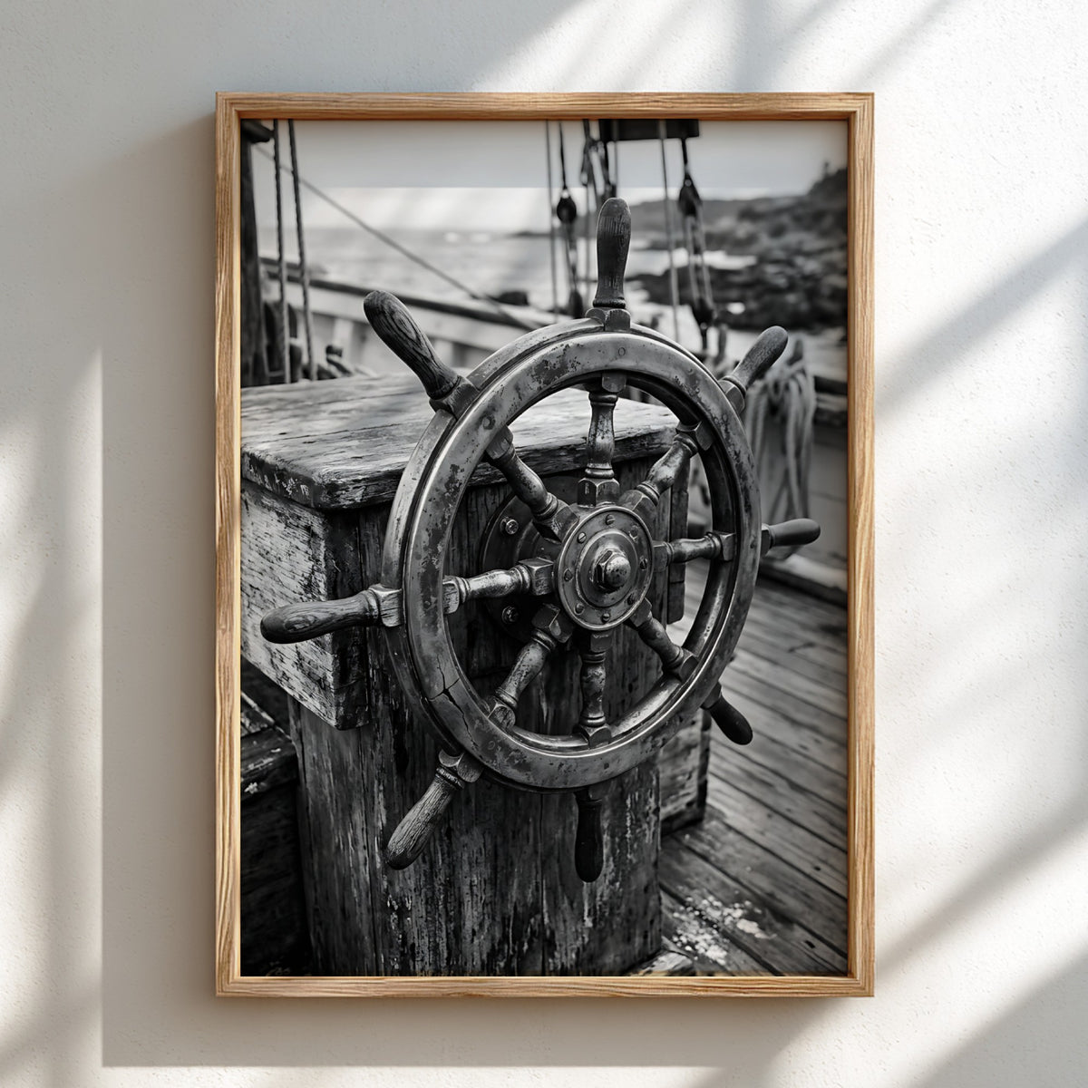Black and white wall decor showing brass ship wheel on wooden deck with nautical ropes