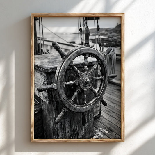 Black and white wall decor showing brass ship wheel on wooden deck with nautical ropes