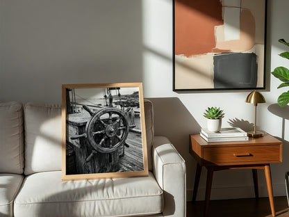 Black and white wall decor showing brass ship wheel on wooden deck with nautical ropes