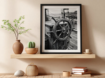 Black and white wall decor showing brass ship wheel on wooden deck with nautical ropes