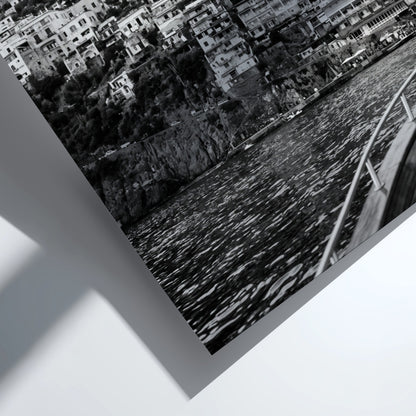 Black and white poster of cliffside village viewed from boat with coastal houses and mountain background