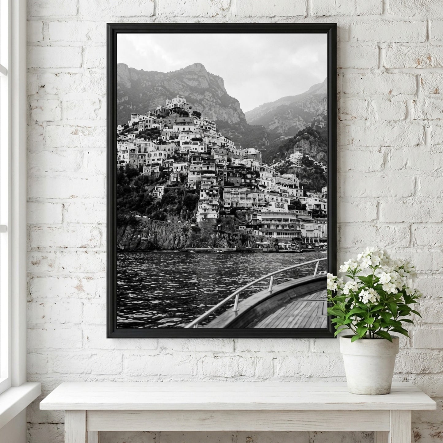 Black and white poster of cliffside village viewed from boat with coastal houses and mountain background