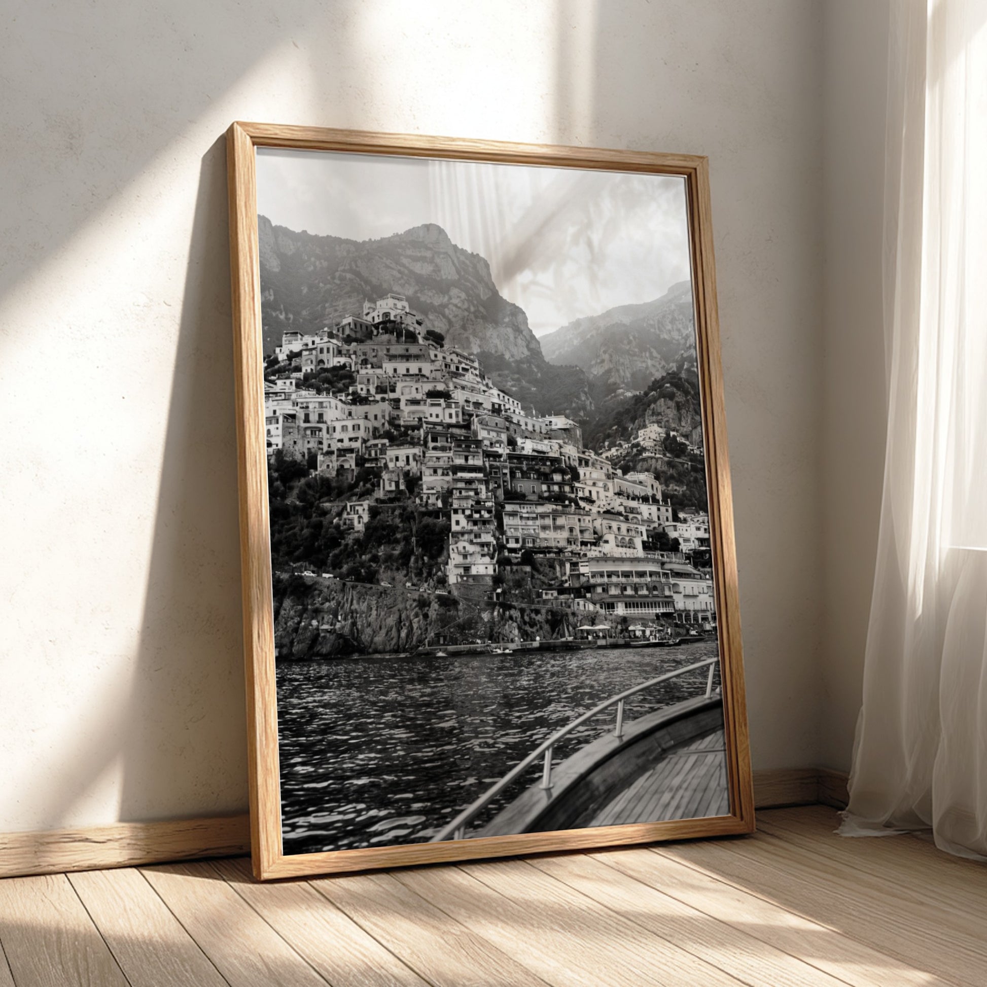 Black and white poster of cliffside village viewed from boat with coastal houses and mountain background