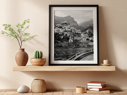 Black and white poster of cliffside village viewed from boat with coastal houses and mountain background