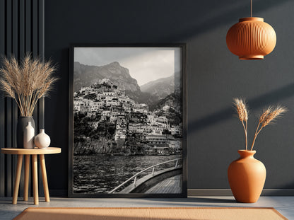 Black and white poster of cliffside village viewed from boat with coastal houses and mountain background