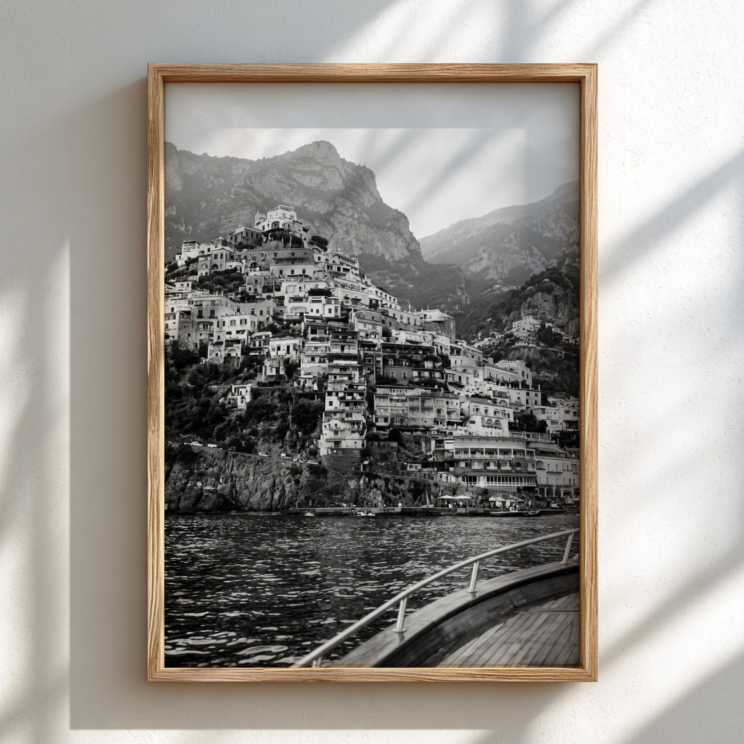 Black and white poster of cliffside village viewed from boat with coastal houses and mountain background