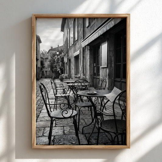 Black and white poster of outdoor cafe table with cup on cobblestone street and iron chairs