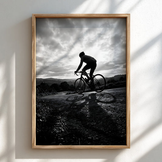 Black and white wall decor of cyclist cresting hill against dramatic cloudy sky silhouette