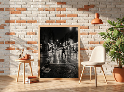 Black and white urban wall decor showing figure crossing wet street at night with reflective asphalt and