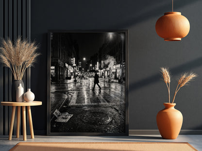 Black and white urban wall decor showing figure crossing wet street at night with reflective asphalt and