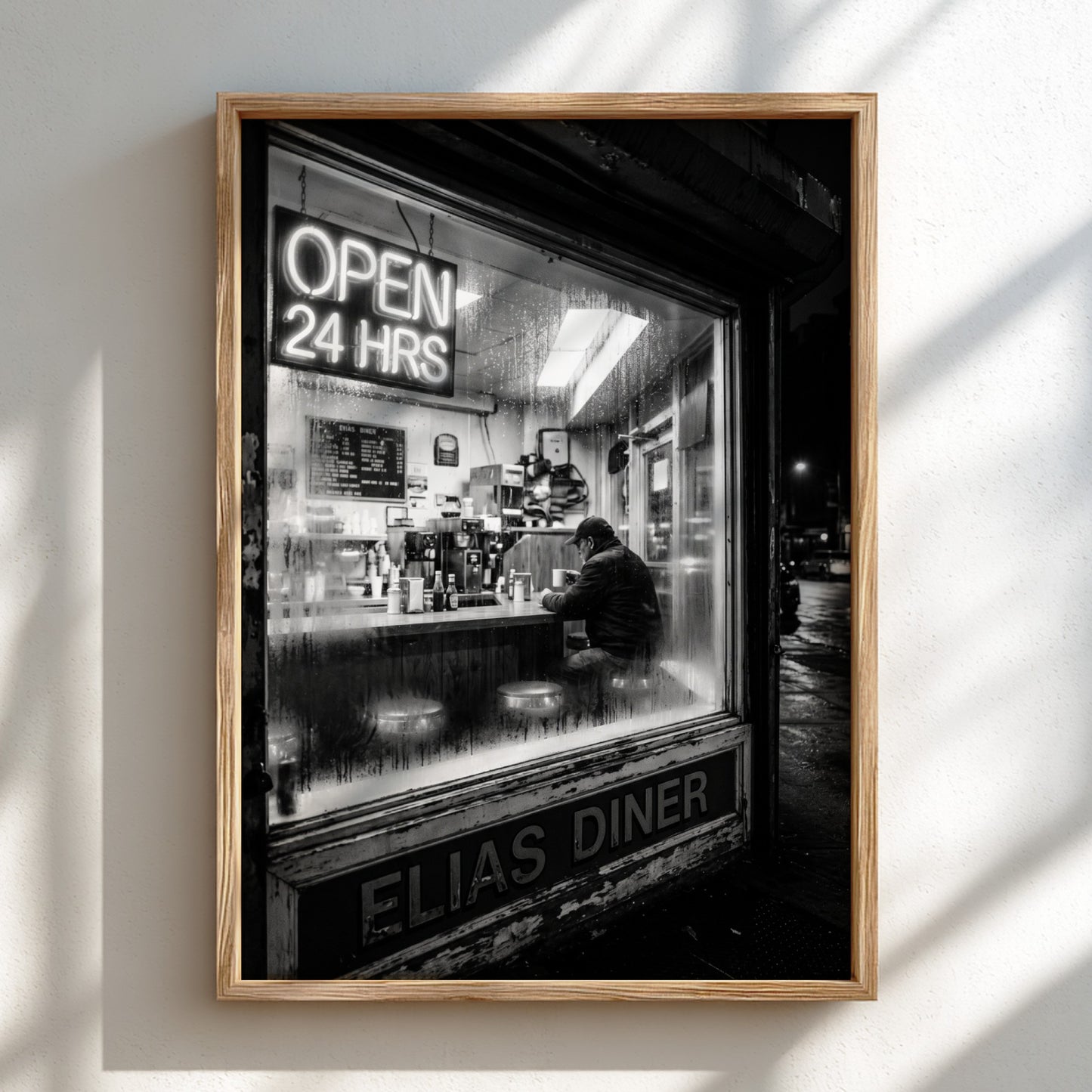Poster of black and white diner interior with neon open 24 hrs sign and lone figure sitting