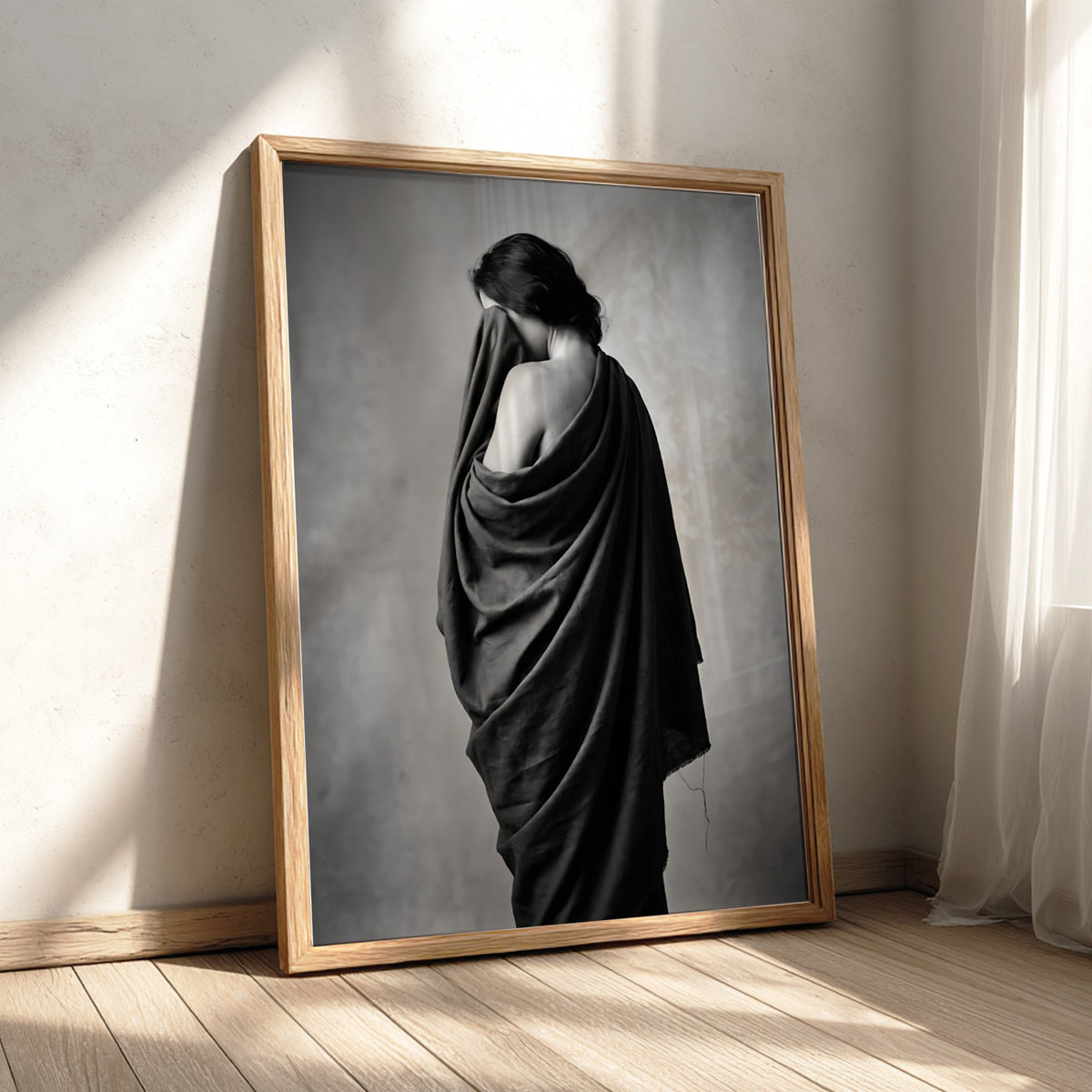 Black and white wall decor of a model draped in flowing dark fabric with soft shadows