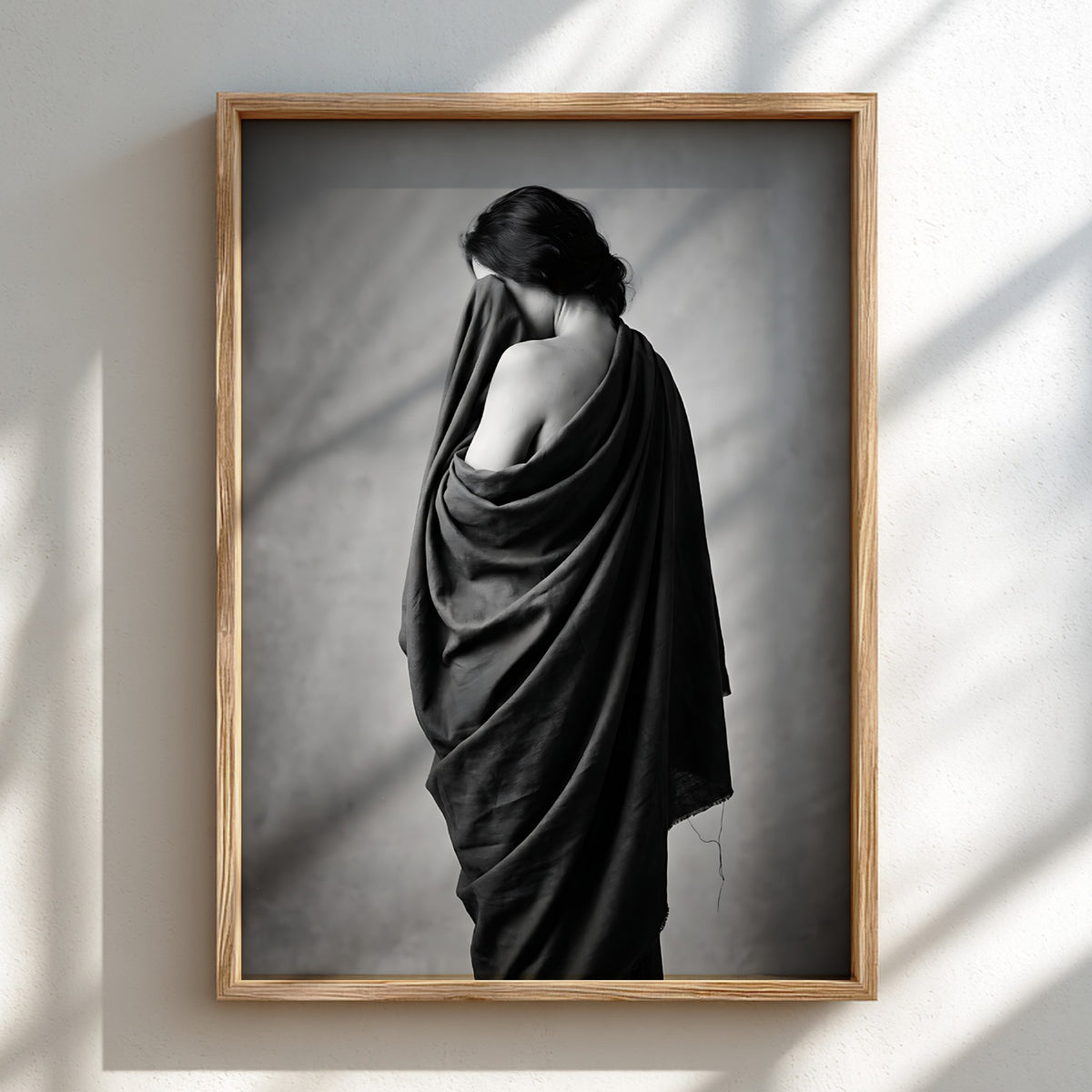 Black and white wall decor of a model draped in flowing dark fabric with soft shadows