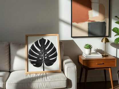 Wall decor featuring a black Monstera leaf with backlit studio effect and natural wood frame on white