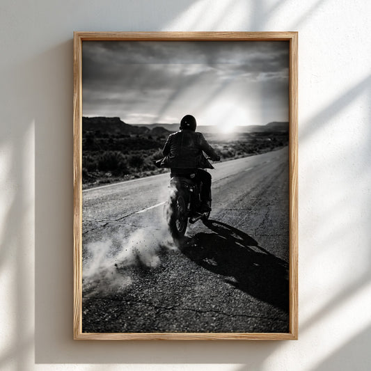 Black and white photographic wall decor of motorcyclist riding on open road with dust and shadows