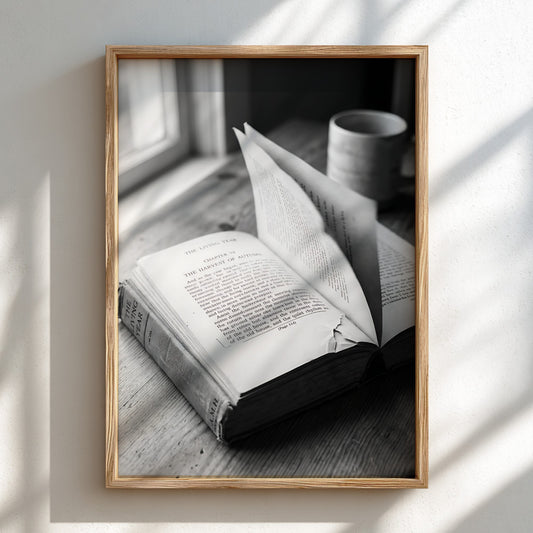 Black and white wall decor showing an open book with pages turning on a wooden surface with soft natural light