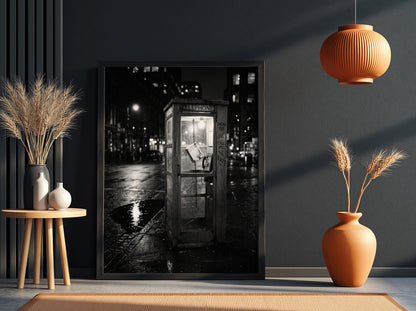 black and white wall decor of illuminated phone booth on rainy city street corner at night