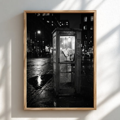 black and white wall decor of illuminated phone booth on rainy city street corner at night
