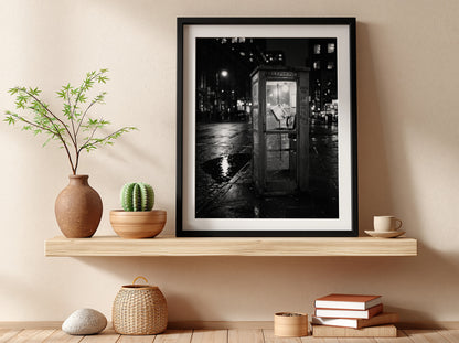 black and white wall decor of illuminated phone booth on rainy city street corner at night