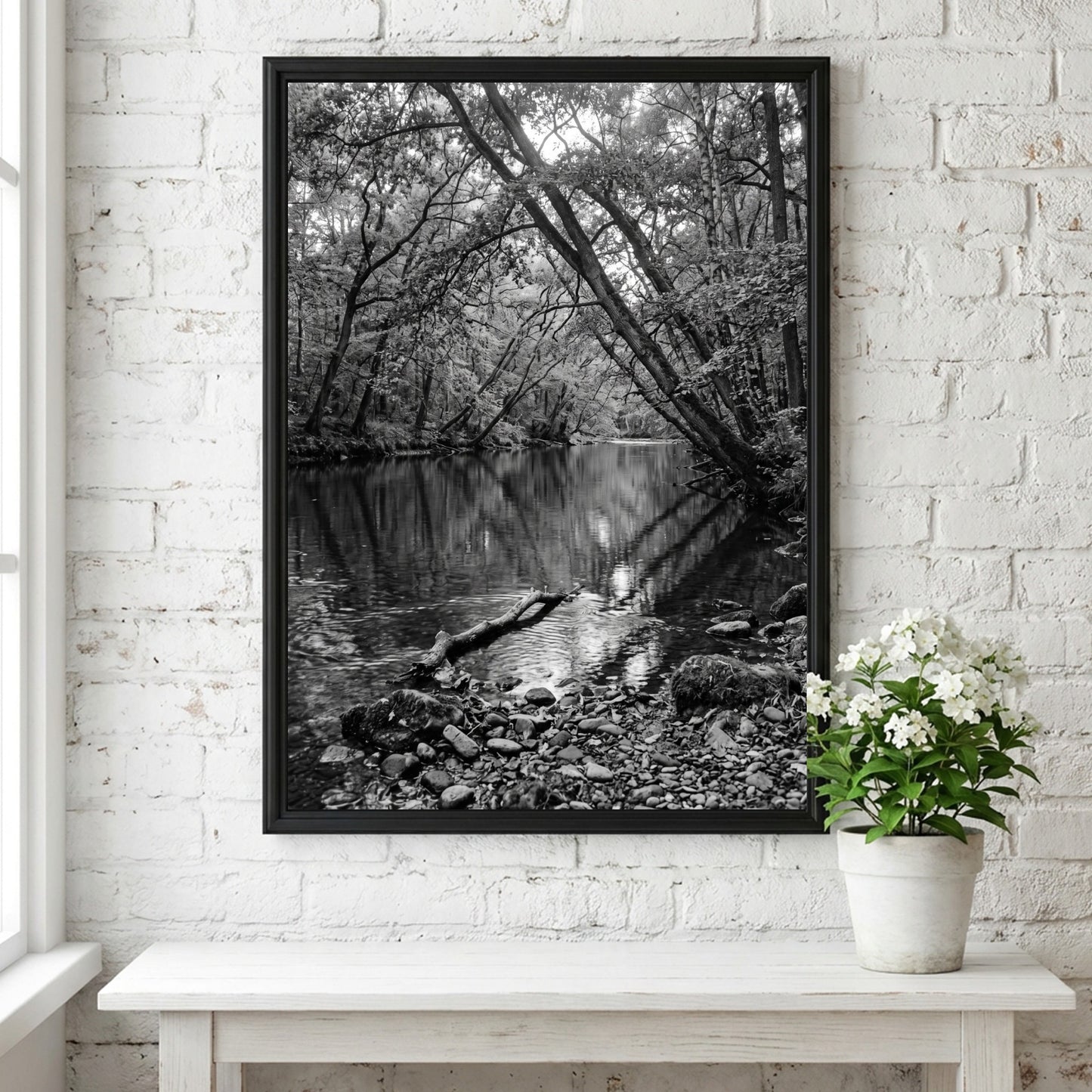 Black and white wall decor featuring trees leaning over a forest river with rocky shore and reflective water