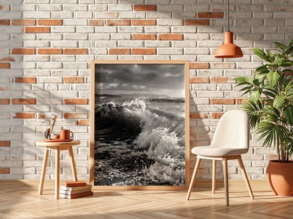Black and white poster of a breaking wave on rocky beach with splashing water and moody sky