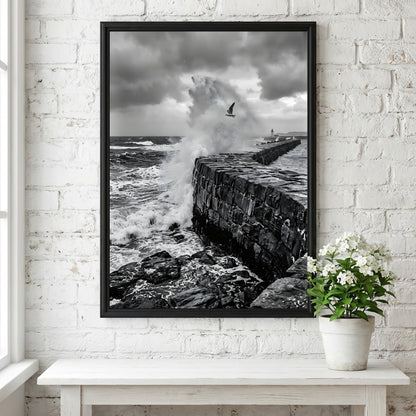 Black and white poster of waves crashing against rugged stone wall under cloudy sky with seagull flying