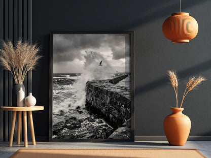 Black and white poster of waves crashing against rugged stone wall under cloudy sky with seagull flying