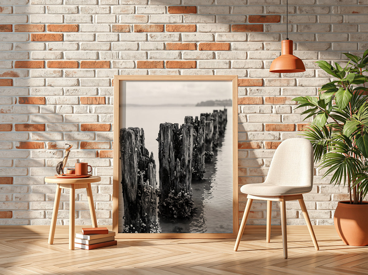 Black and white wall decor photograph of weathered wooden pier pilings in calm water with marine growth